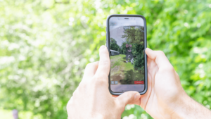 Two hands holding an iPhone with an augmented reality Brian Brooks dancing on the great lawn.