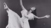A black and white image of Yuriko, who extends her right leg in the air, tilts her head back, and opens her arms, right arm raised to the sky. Yuriko wears a white dress and her hair is long and runs down her back.