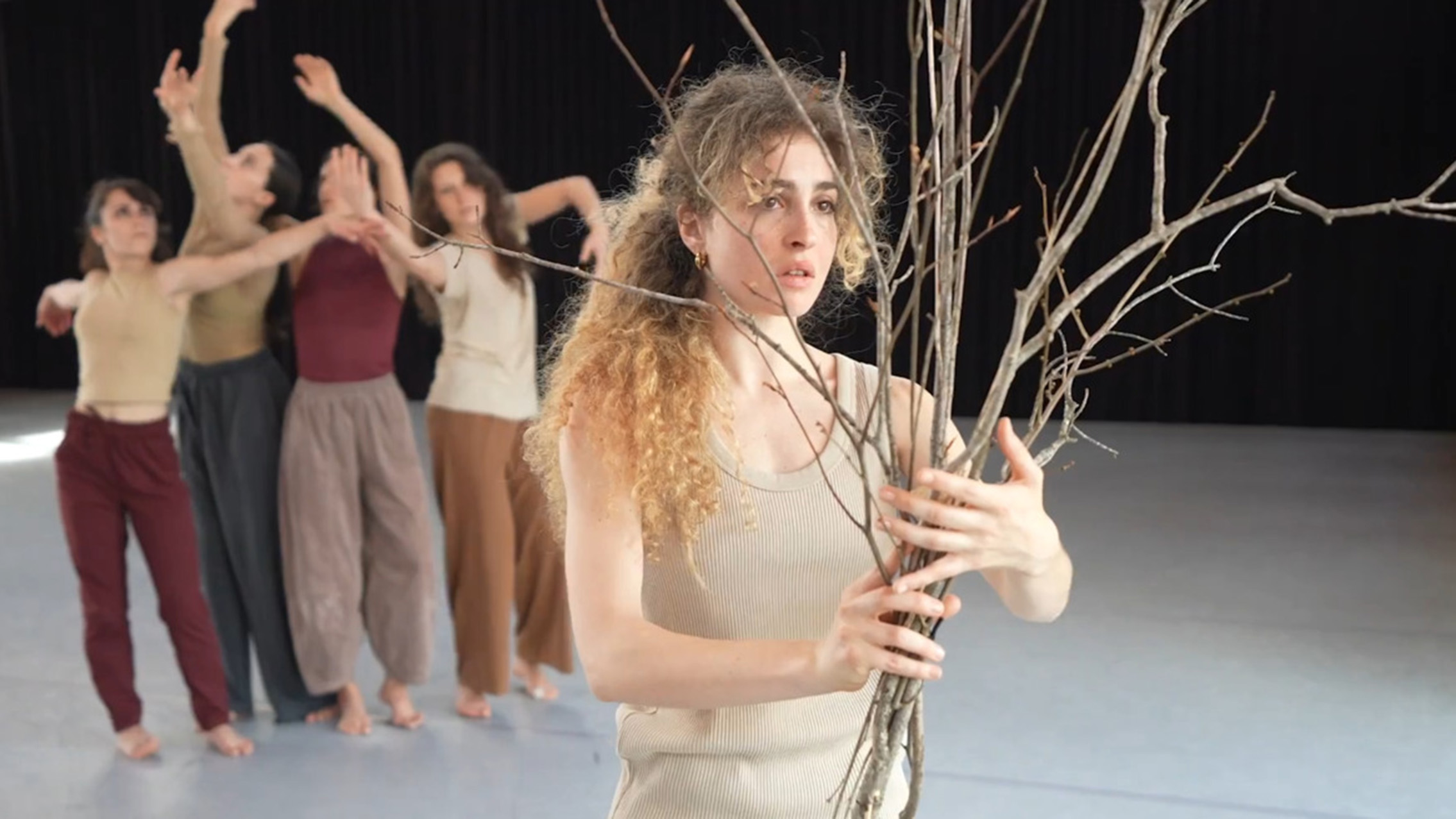 A dancer is in focus holding a collection of sticks while four dancers are behind them in a clump.