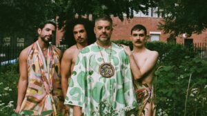 Miguel Gutierrez posing straight to the camera with 3 other artist around them all dressed in flowy lose fitting clothing.