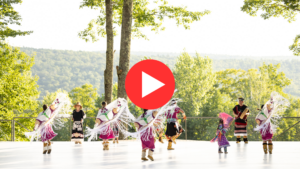 A dancer in Indigenous regalia from Northwestern British Columbia dances on an outdoor stage.