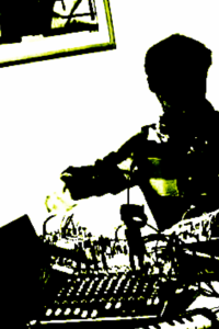 A heavily computer-processed, pixelated, high contrast black and white image with fringes of green color of Colin performing on a musical instrument consisting of a tangle of wires and controls.